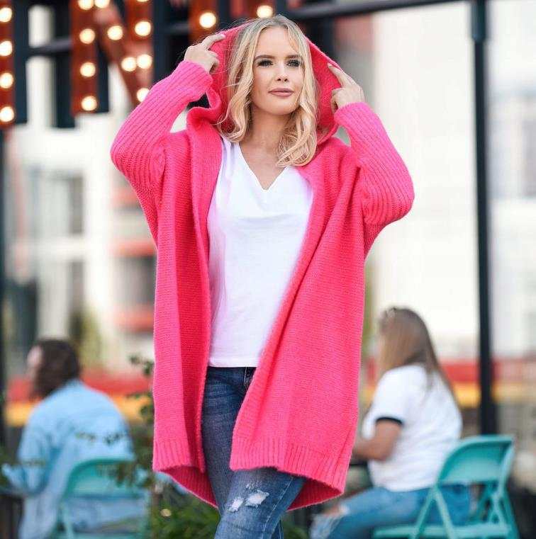 Woman wearing a bright pink oversized bat sleeve hooded cardigan with a white top and ripped jeans outdoors