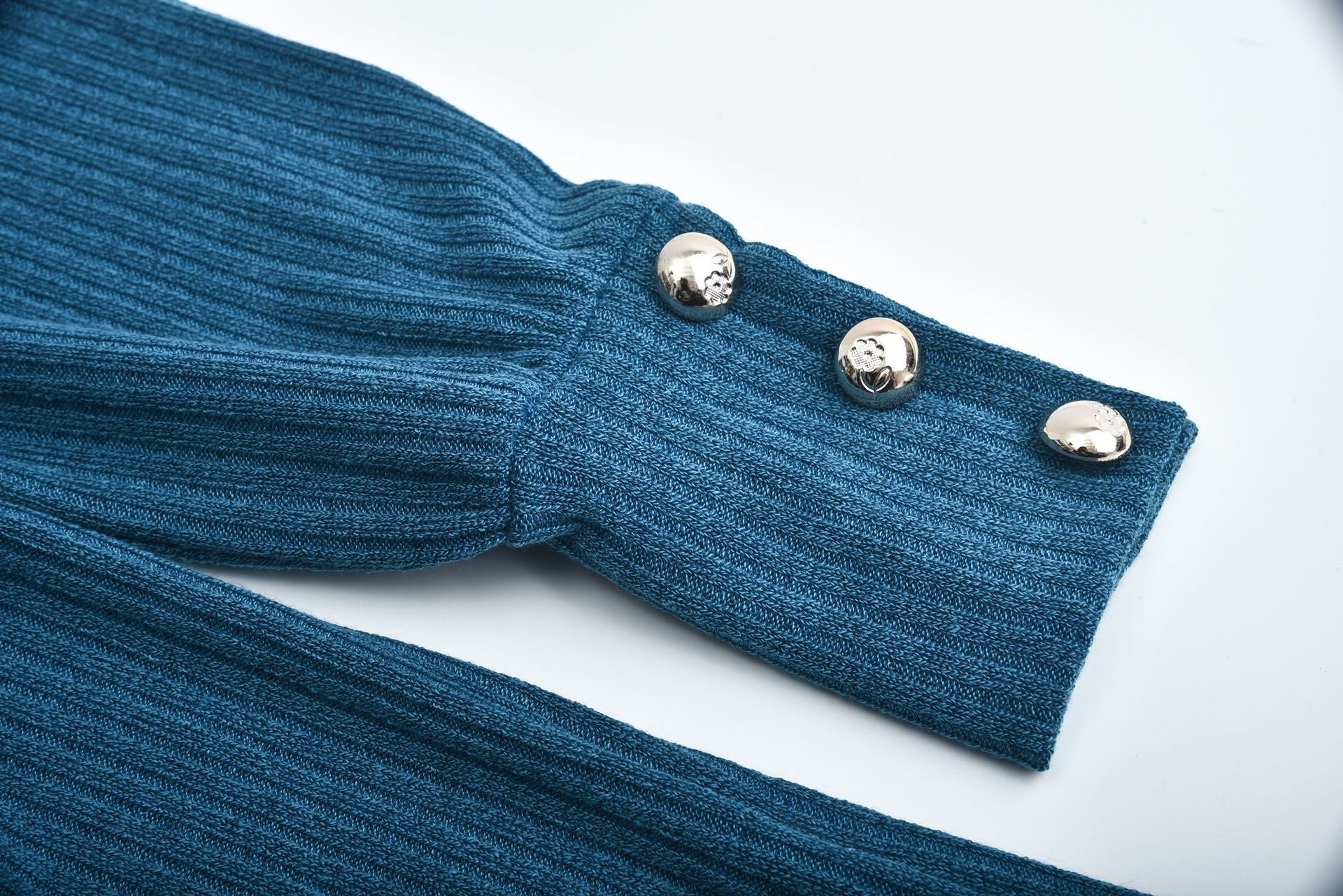Close-up of blue ribbed cotton blend women's lapel pullover sleeve with three silver buttons