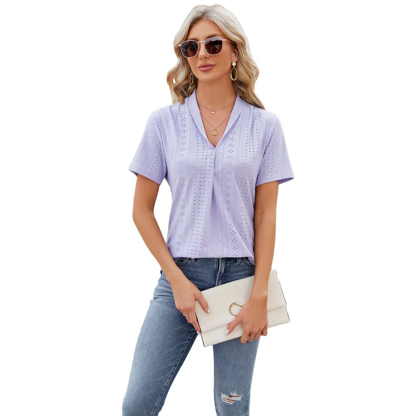 Woman wearing lavender V-neck hollow design T-shirt with short sleeves and casual fit holding a white clutch and sunglasses