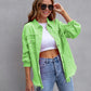 woman wearing bright green ripped shirt jacket with white crop top and blue jeans standing against gray wall