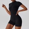 Woman wearing black zipper short sleeve yoga jumpsuit with tight fit and pullover style
