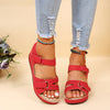 Red wedge sandals with velcro straps worn with ripped jeans on a beige background