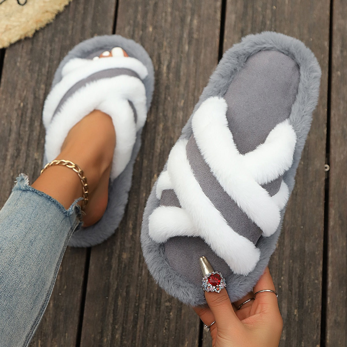 Gray and white fluffy slippers with cross strap stitching on wooden floor