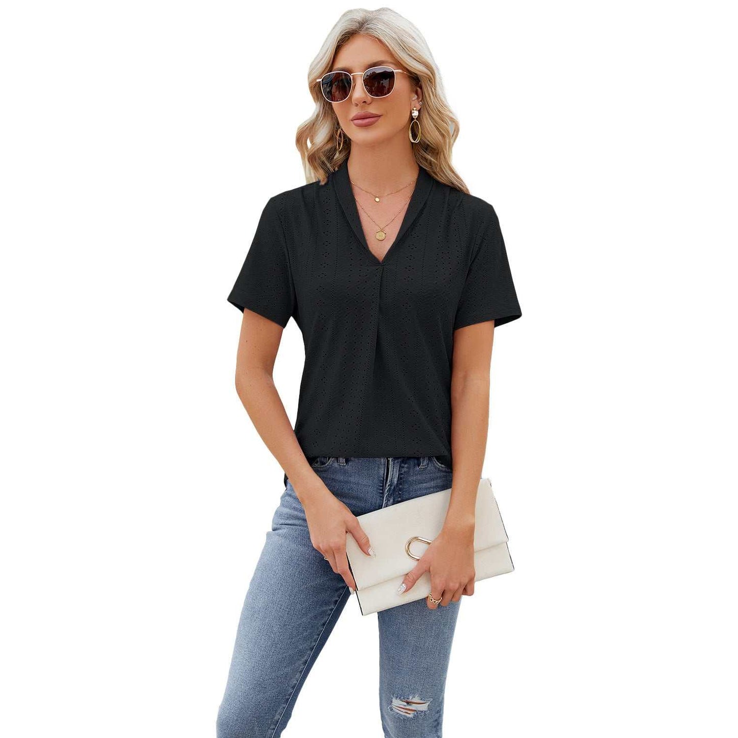 Woman wearing black V-neck hollow design T-shirt with short sleeves and blue jeans, holding a beige clutch bag