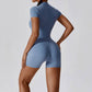 Woman wearing haze blue zipper short sleeve yoga jumpsuit with tight waist-length fit and pullover style