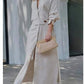 Woman wearing elegant tied solid color waisted long-sleeved shirt dress with slit and holding woven clutch.