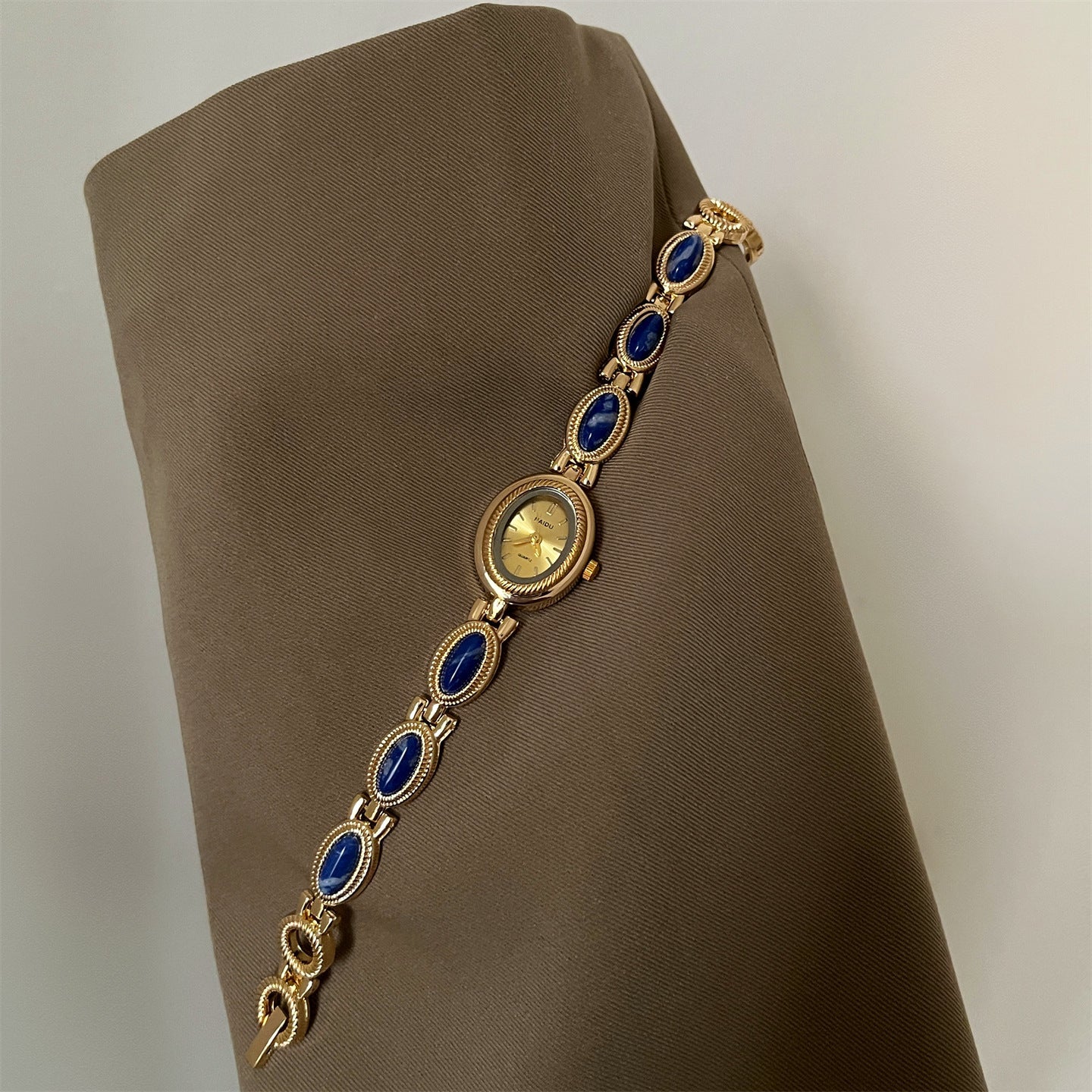 Women's agate bead bracelet watch with gold-tone alloy and blue oval stones on brown fabric background