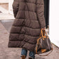 Woman wearing a solid color hooded long winter coat with long sleeves and mid-length design walking outdoors