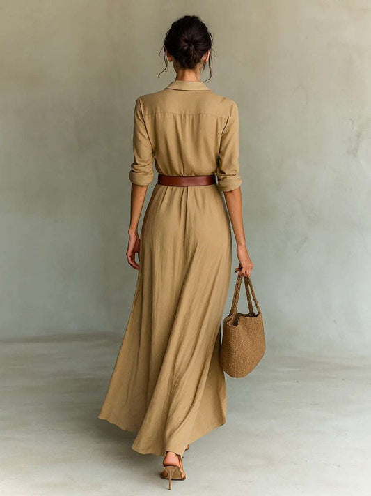 Woman wearing khaki irregular long dress with belt and long sleeves, holding a woven handbag, shown from the back