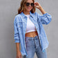Woman wearing light blue ripped shirt jacket with frayed edges over white crop top and jeans