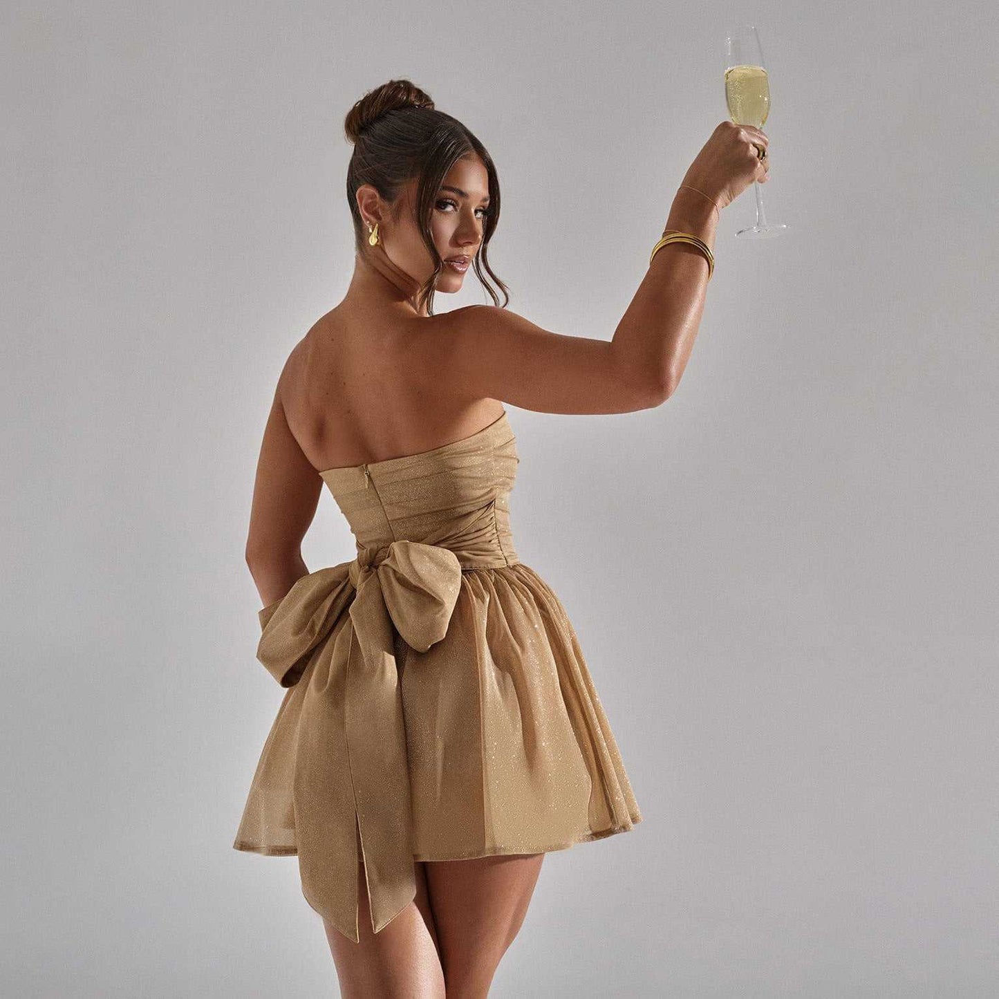Woman wearing beige tube top lace dress with back bow-knot holding a champagne glass