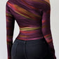 woman wearing a slim fit print long sleeve t-shirt with asymmetrical neckline and ruched sides in purple and orange tones