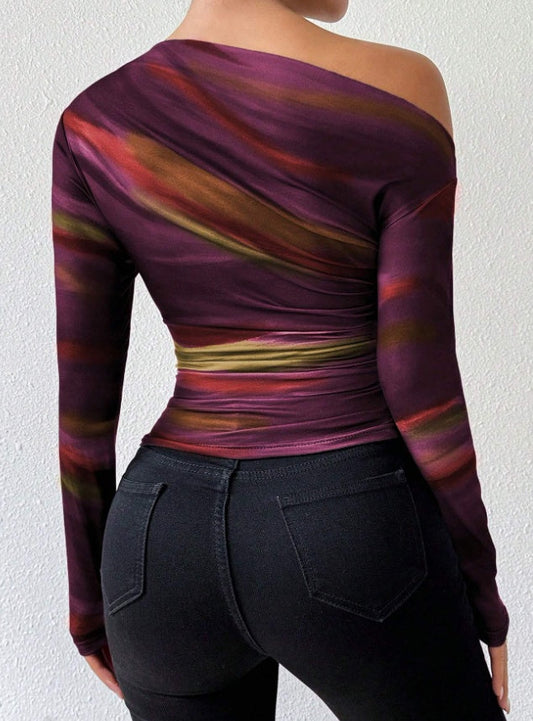 woman wearing a slim fit print long sleeve t-shirt with asymmetrical neckline and ruched sides in purple and orange tones