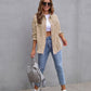 Woman wearing beige ripped shirt jacket with blue ripped jeans and white sneakers standing against gray wall