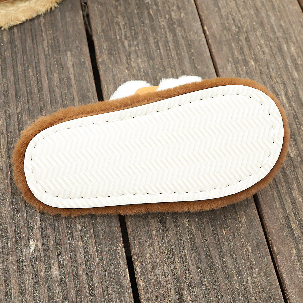Bottom view of brown fluffy slippers with white EVA sole on wooden floor