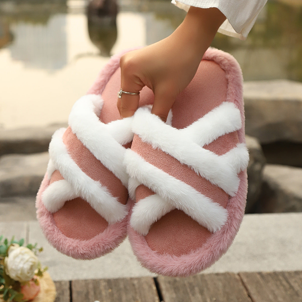 Pink fluffy slippers with cross strap and white stitching held by hand outdoors