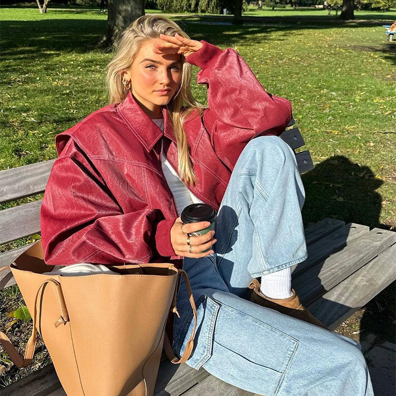 Woman wearing loose fashion lapel red zip-up jacket sitting on a bench outdoors