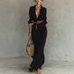 Woman wearing elegant black irregular long dress with belt and button lapel, carrying woven bag, styled for office or daily wear