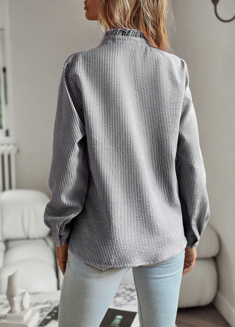 Back view of a woman wearing a gray striped long sleeve shirt with ruffle collar and button-up design, styled casually with light blue jeans.